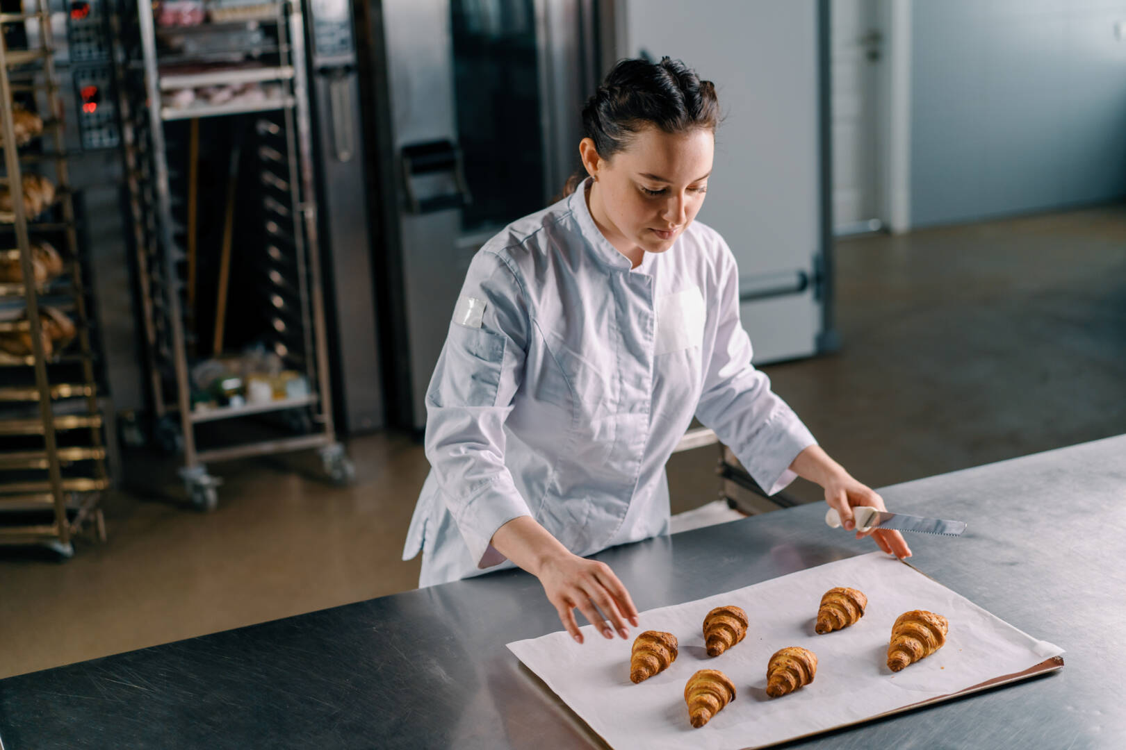 attractive baker puts a baking sheet on the table with ready freshly baked hot fragrant buns baking production bakery